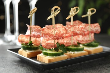 Tasty canapes with salami, cucumber and cream cheese on grey table, closeup