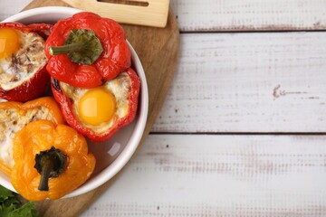 Delicious stuffed peppers with eggs in bowl on white wooden table, top view. Space for text