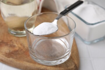 Baking soda in spoon, glass bowl and vinegar on white table, closeup