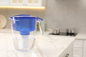 Water filter jug on white marble table in kitchen, space for text