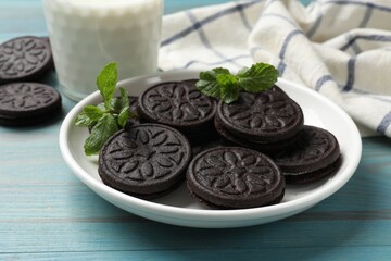 Plate with tasty sandwich cookies and mint on light blue wooden table, closeup