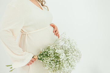 Beautiful young pregnant woman with on white background. Stylish pregnant woman in beige dress. Motherhood. Mother's Day.