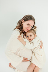 Beautiful young pregnant woman with her little 3 yearold daughter on white background. Stylish pregnant woman in beige dress. Motherhood. Mother's Day.