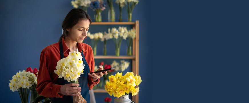 happy florist woman standing with bouquet of flowers in workshop using mobile phone for social networks.