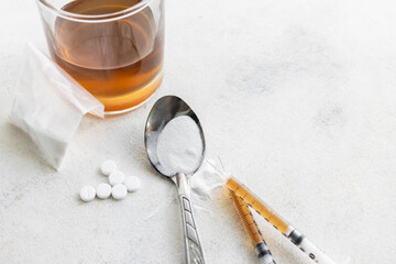 Narcotic substances in spoon, dope powder in transparent plastic bag, syringes with drugs dose, white pills and glass of alcohol drink on textured background. Concept of addiction and bad habits