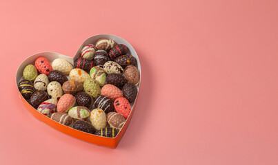 Assorted gourmet of Chocolate Easter eggs in a heart-shaped box on a rose background.
