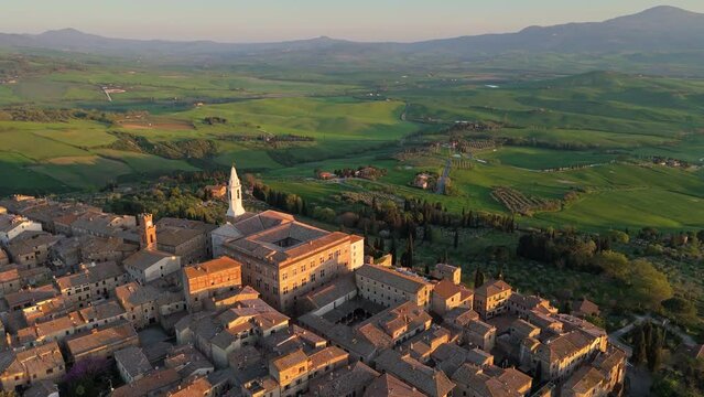 Flying over Pienza old town, Tuscany green hills on background. Aerial sunset view of Pienza medieval village, Tuscany, Italy