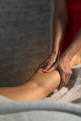 Close-up of a masseur in a red suit massaging the calf muscle of a young woman. Spa massage in a...