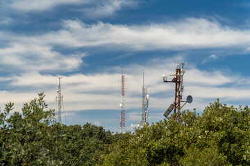 Telecommunication antennas over the trees on a sunny day with clouds.