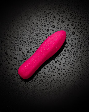 Pink bullet vibrator sprinkled by water drops on dark backdrop