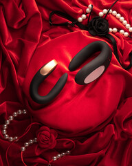 Set of Stylish black vibrators and colorful silicone anal plugs arranged on red satin with flowers...
