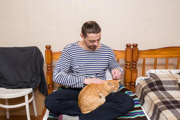 A man strokes a ginger cat with his hand.