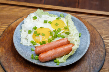 Scrambled two eggs with sausages sprinkled with green onions on a gray plate