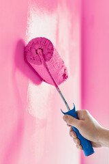 Close-up on the hand of a man who is painting a wall pink with a paint roller. Painting apartment, renovating with pink color paint.