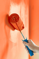 Close-up on the hand of a man who is painting a wall red orange with a paint roller. Painting apartment, renovating with red orange color paint.