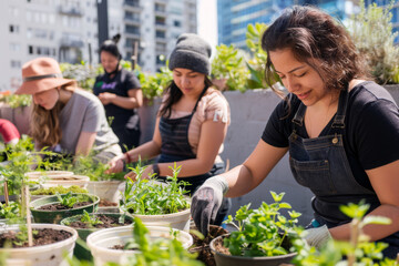 Urban gardening workshop on a sunny rooftop. Diverse group of people of different ages and ethnicities planting herbs and small vegetables in recycled containers