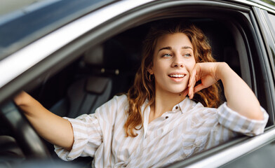 Young smiling woman driving a car drives around the city. Car travel, lifestyle, carshering concept.