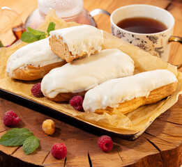Sliced raspberry cream Swiss roll adorned with pink icing and nut crumbs, nestled among fresh berries with backdrop of warm tea. Inviting moment of indulgence at teatime spread