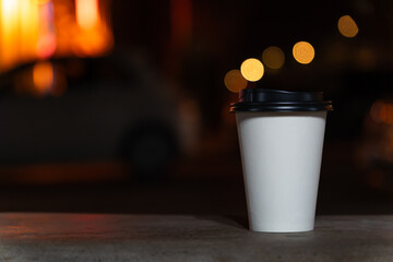 Close-up of a disposable white paper cup with coffee or tea stands on a bench against the...