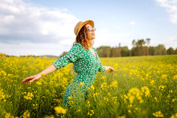 Fototapeta premium Beautiful woman in bright dress in rapeseed field. Nature, vacation, relax and lifestyle. Summer landscape.