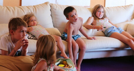 Many children seated a living room sofa watching TV kids together at play room