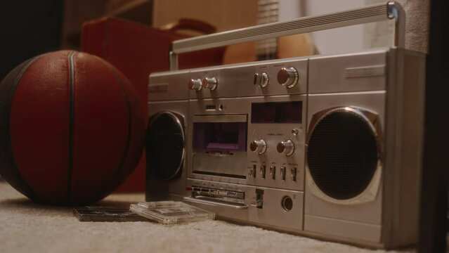 No people footage of light gray boombox player or jambox on carpeted floor by two cassettes and basketball indoors, nostalgic 90s