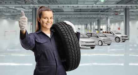 Woman mechanic worker carrying a car tire and gesturing a thumb up sign