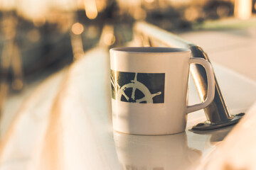 White cup with drawn helm on deck of a white yacht, ship, boat. Concept of tea coffee drinking...