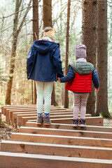 Zwei Kinder laufen auf Holzstamm im Wald. Kinder unterstützen sich gegenseitig bei...