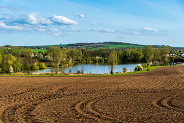 Spring field freshly plowed field in landscape with pond and hills.