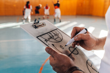 Elderly male basketball coach drawing his strategy on a coach clipboard