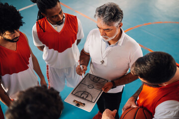 Mature basketball coach drawing defense on a clipboard to his diverse team