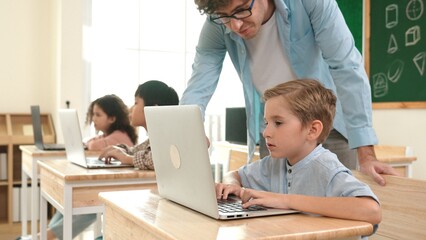 Caucasian teacher helping energetic boy coding engineering prompt while diverse student using...