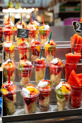 Fruit Salad arranged in plastic cups on a market. Cut and ready fruit ready to sell in market. Convenience, healthy lifestyle. Strawberries, kiwi, melon, pineapple, coconut, dragon in a plastic glass.