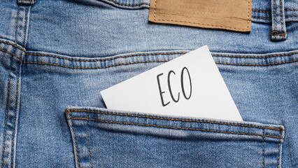  White card with a handwritten inscription "Eco", inserted into the pocket of blue pants jeasnow (selective focus)