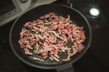Many bacon dices being fried and cooked on a black pan
