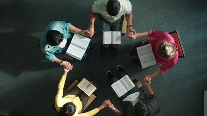 Top down view of diverse people holding hand and sitting in circle with bible book on lap. Aerial...