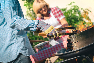 Senior couple preparing barbecue in backyard on a sunny day. Man holding a food grab while wearing...