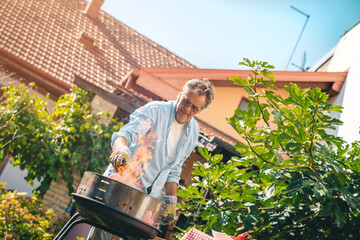 Senior adult male preparing barbecue in backyard on a sunny day. Focused older man wearing shirt...