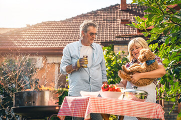 Cheerful senior couple playing with dog while making barbecue in backyard on a sunny day. Woman...