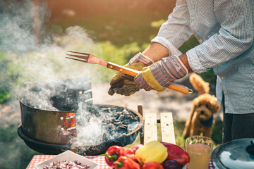 Close up of a male preparing barbecue in backyard. Unknown man with protective gloves holding fork...