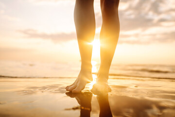Slim female legs and feet walking along sea water waves on sandy beach. Pretty woman walks at...