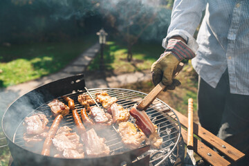 Close up photo of man preparing meat on the grill in his backyard. Male person picking up roasted...