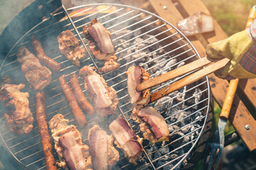 Close up photo of different kind of meat on the grill grid. Unknown male or female grilling bacon...