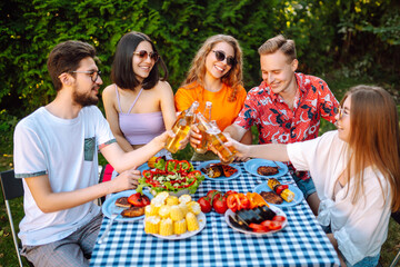 Group of friends sitting atr table toasting beer glasses in brewery pub garden. Vacation, picnic, weekend, nature.