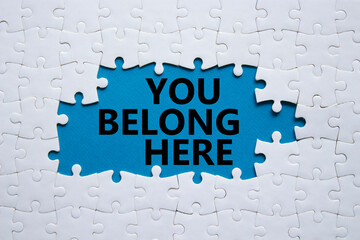 You belong here symbol. White puzzle with words You belong here. Beautiful blue background....