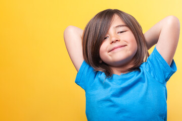 Boy with blue t-shirt and long brown hair puts his hands behind his head in a relaxed pose with a...