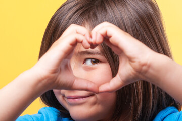 Child makes the shape of a heart with his fingers and hands and looks through it.