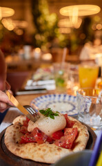 Person preparing bruschetta with tomatoes, egg on a pizza with tableware