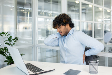 A young professional male experiences sudden back pain at his workspace, reflecting the common issue of workplace ergonomics and health.